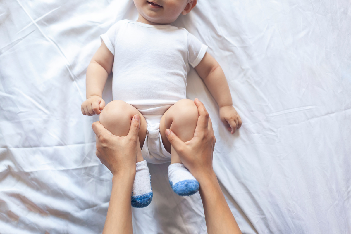 Baby Massage. Mom Doing Gymnastics with Kid. Mommy Massaging Cute Baby Boy. Moving Baby's Legs to Help Relieve Constipation. Young Mother Doing Exercises and Movements to Stimulate Baby's Bowels.